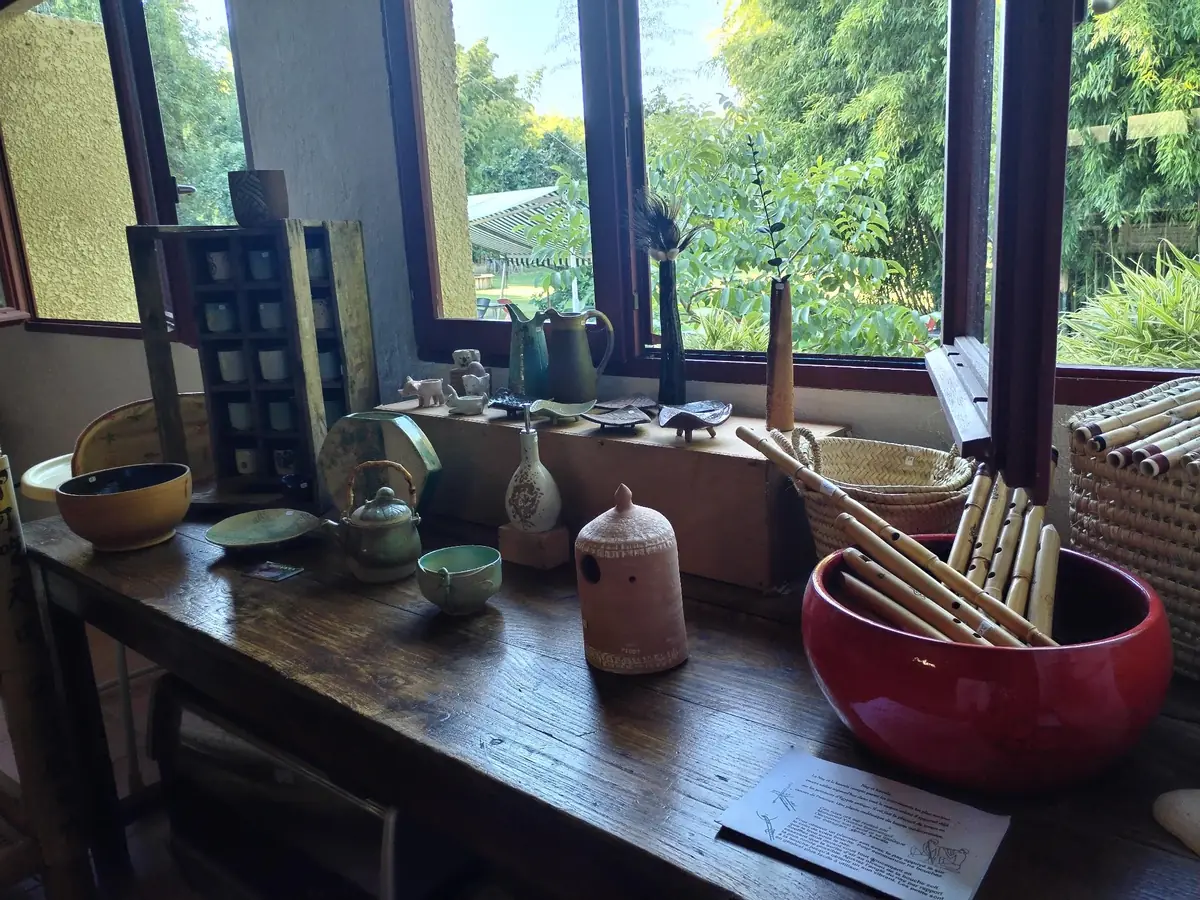 Table de boutique devant les fenêtres du parc, avec vaisselle, panier, bambous et créations artisanales