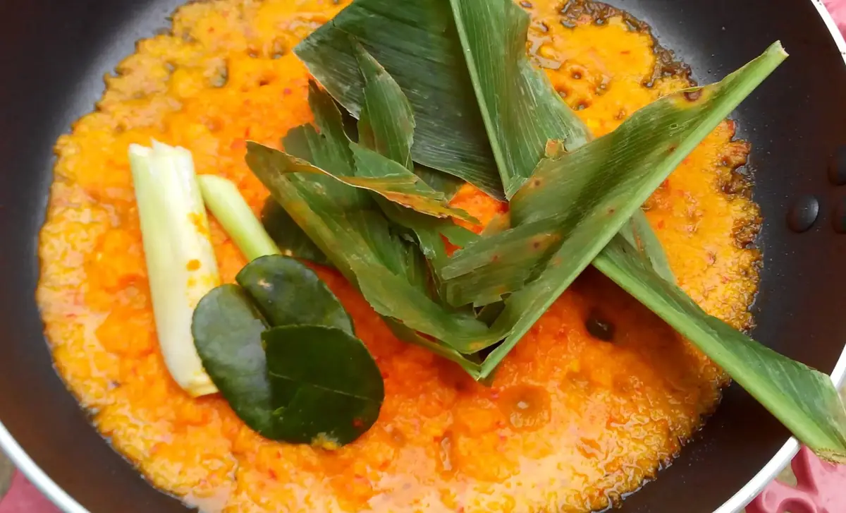 Sauce aux épices en train de réduire dans une poêle, avec citronnelle et feuilles de combava