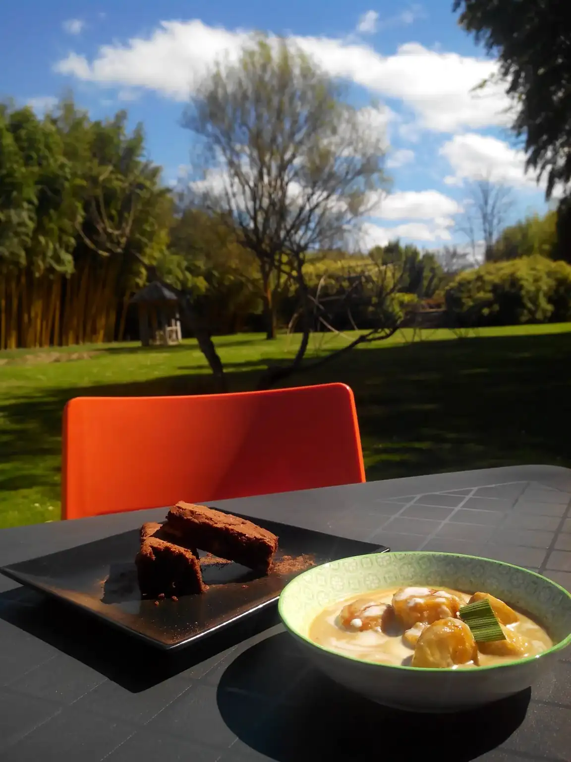 Table du restaurant face à la pelouse et aux bambous du parc, avec un dessert au lait de coco et un gâteau au chocolat